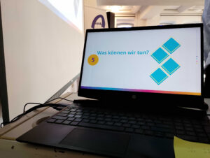 Auf einem Laptop ist eine Folie aus einer Powerpoint-Präsentation zu sehen. Darauf steht die Frage: Was können wir tun?